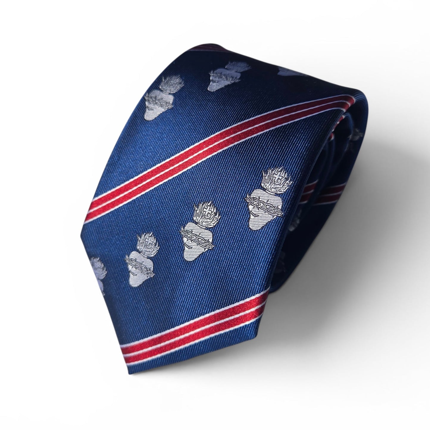 A navy blue silk necktie with diagonal red and white stripes and repeating sacred heart motifs, displayed on a clean white background rolled.