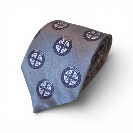 St. Benedict Medal necktie in blue grey with repeating navy blue Benedictine medal medallion pattern, rolled product shot on white background